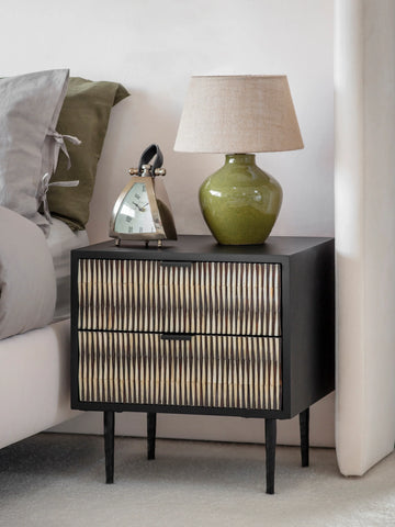 Black bedside table with bone inlay beside bed, topped with green lamp and clock.