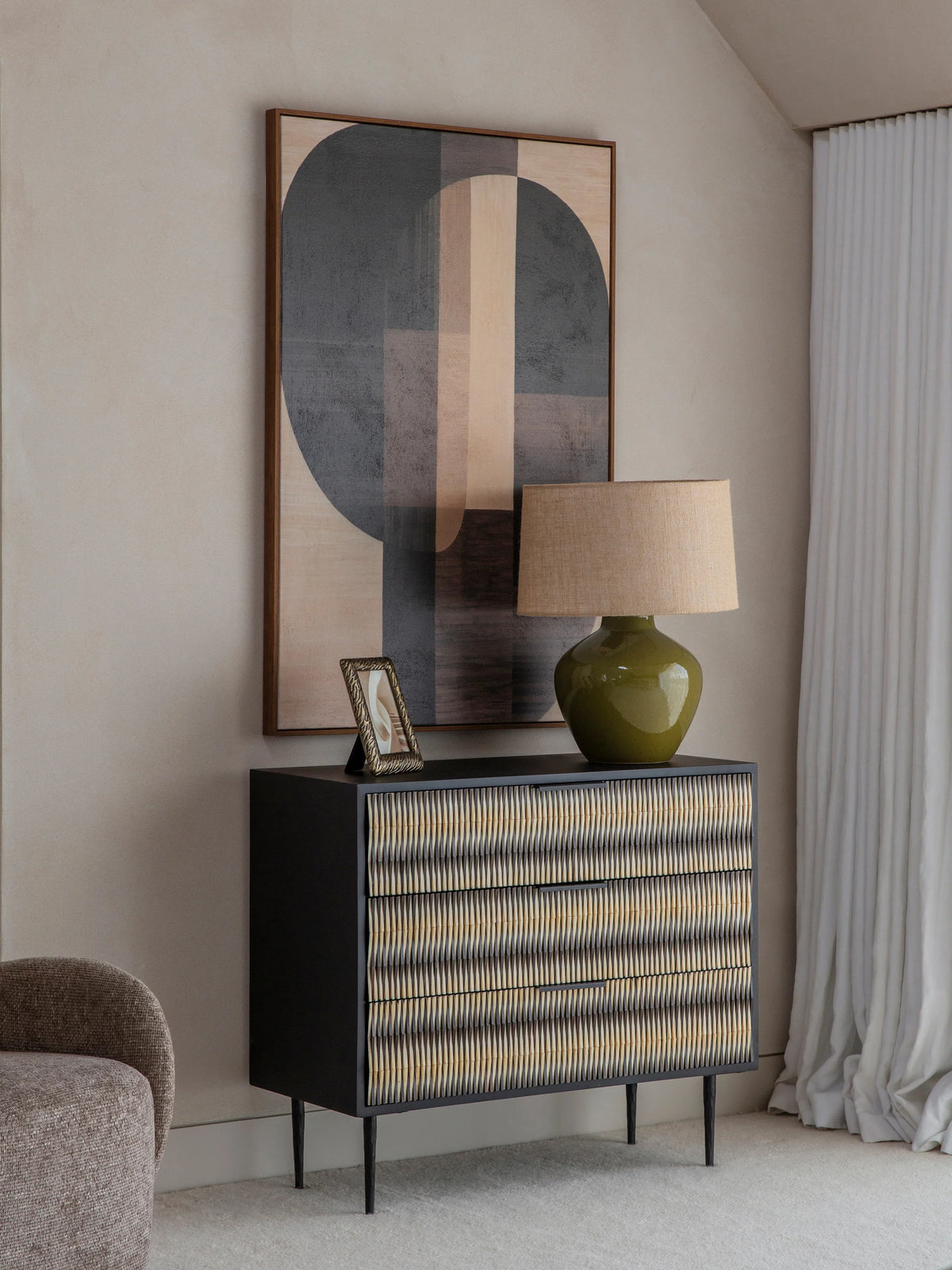 Patterned chest in a modern room with abstract art and a green lamp.