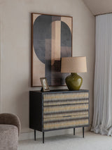 Patterned chest in a modern room with abstract art and a green lamp.