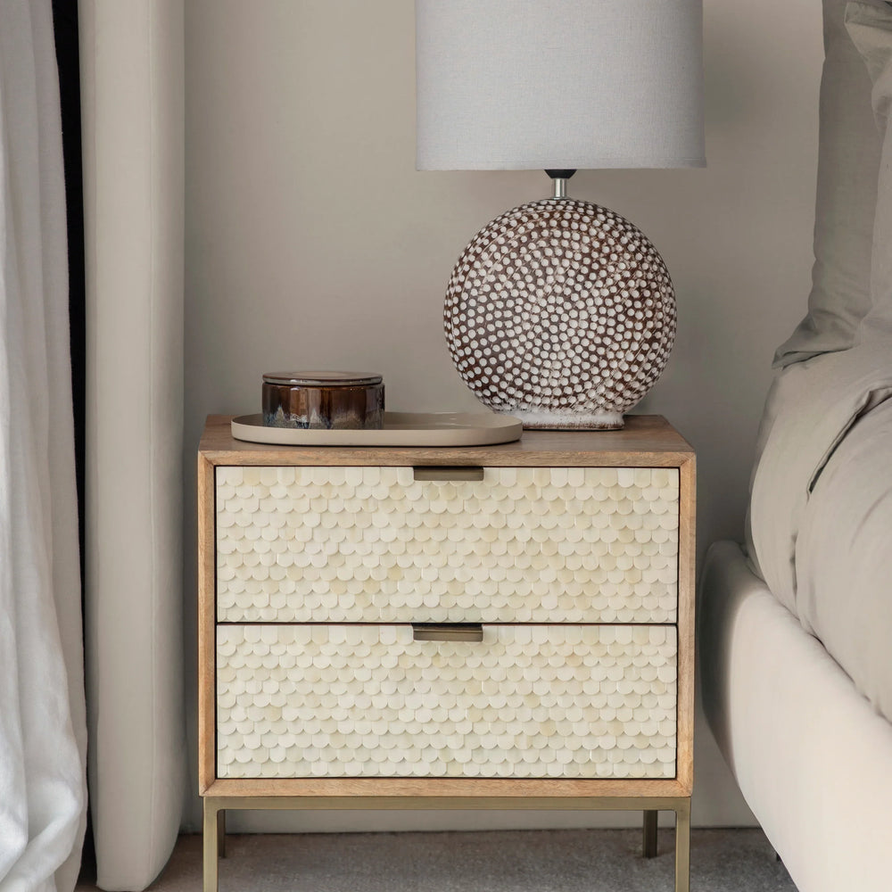 Cream inlay bedside table with textured drawers beside bed and lamp.