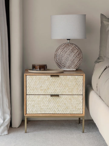 Cream inlay bedside table with textured drawers beside bed and lamp.