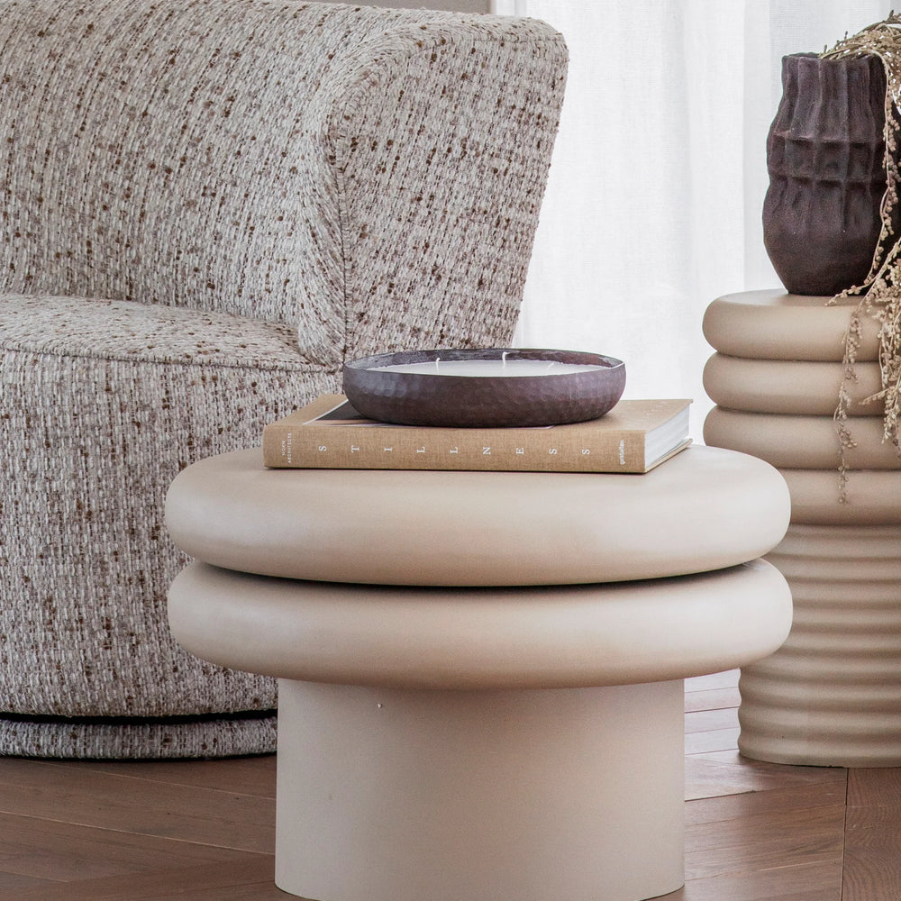 Beige round coffee table with stacked rings, styled in a cozy living room setting.