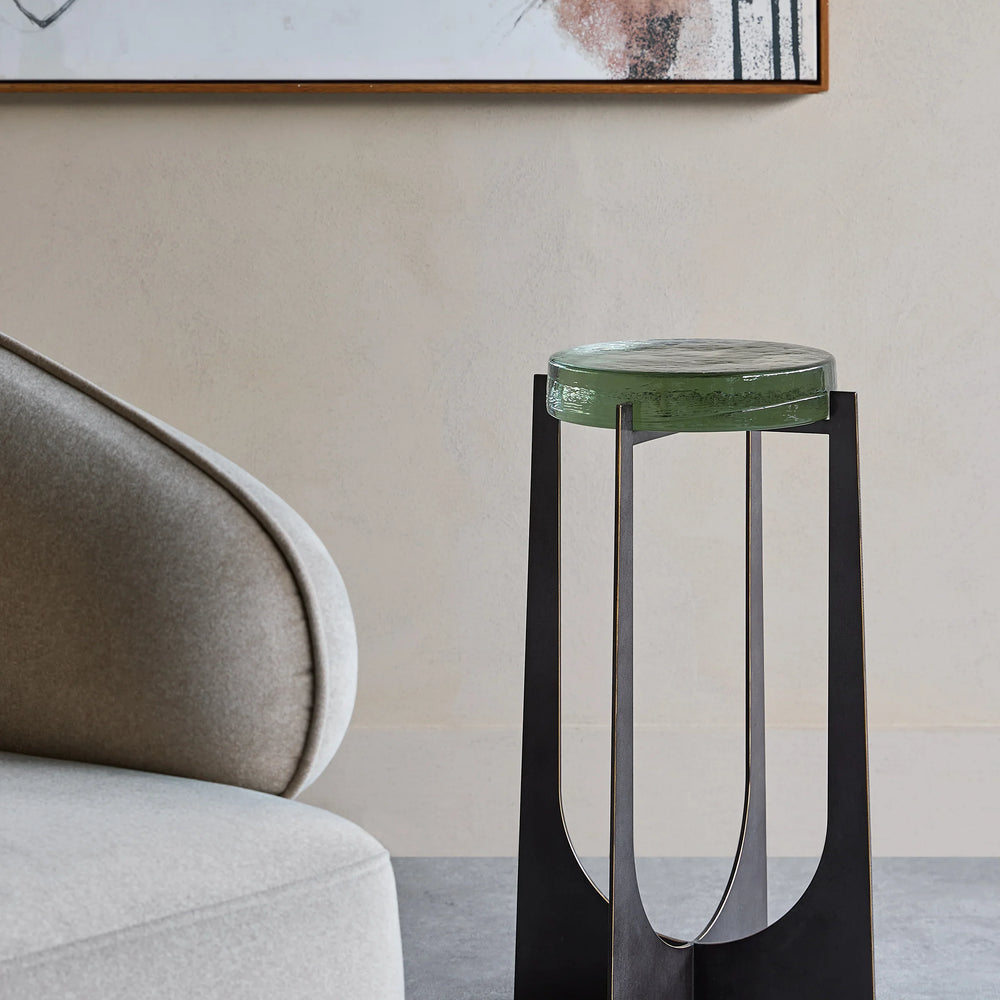 Green glass-topped accent table beside a modern beige chair in a stylish room.
