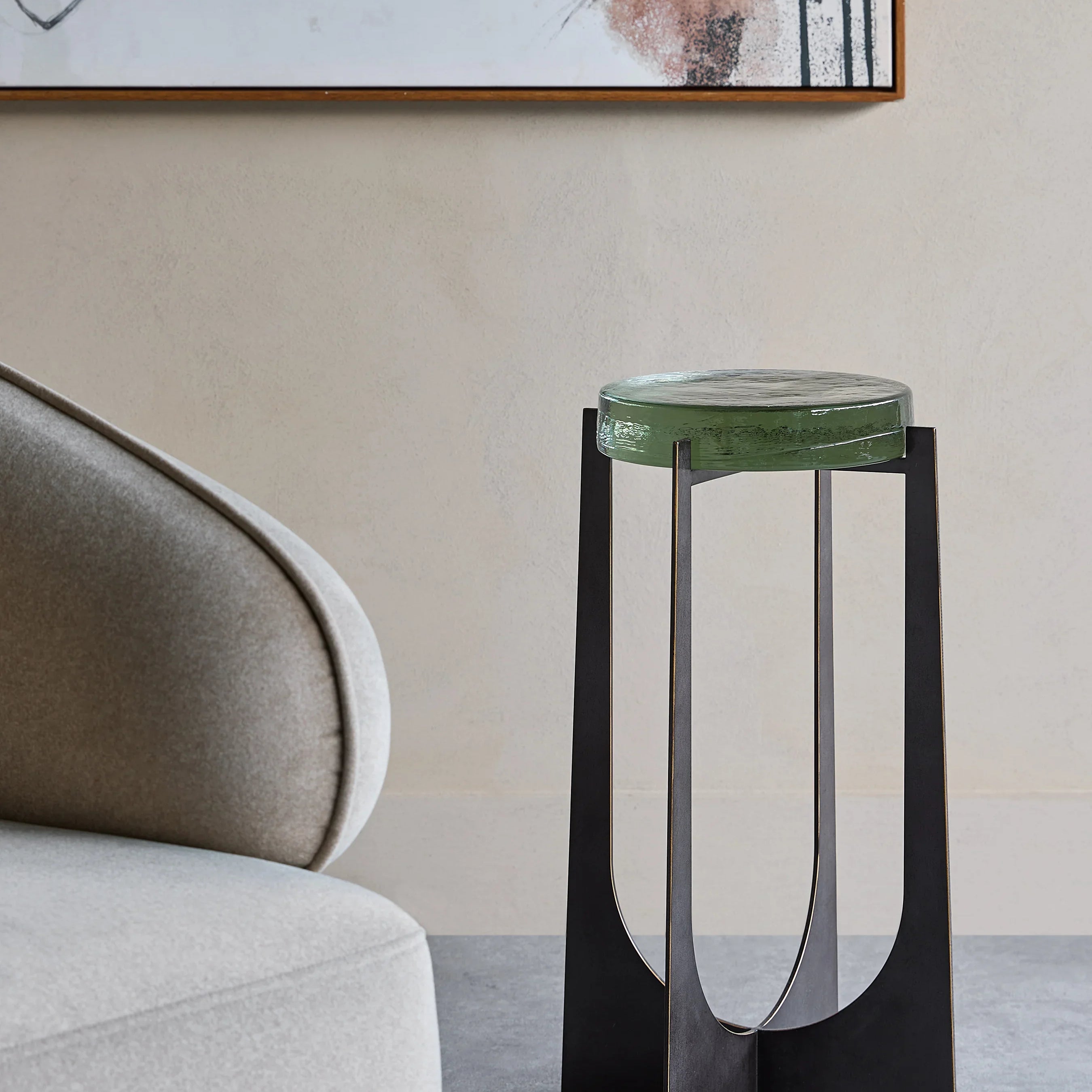 Green glass-topped accent table beside a modern beige chair in a stylish room.