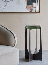 Green glass-topped accent table beside a modern beige chair in a stylish room.