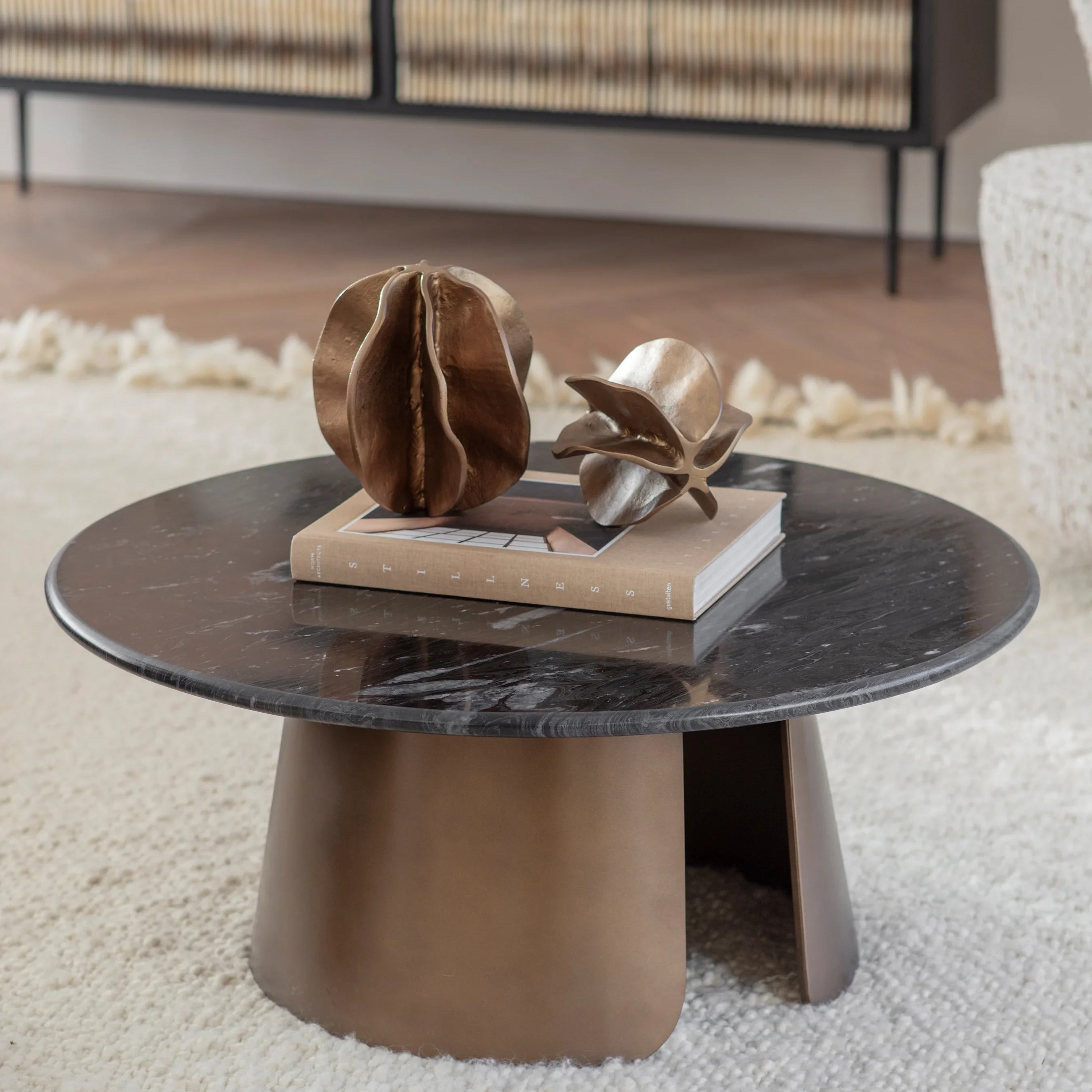 Round marble coffee table with bronze base, styled with decorative sculptures.