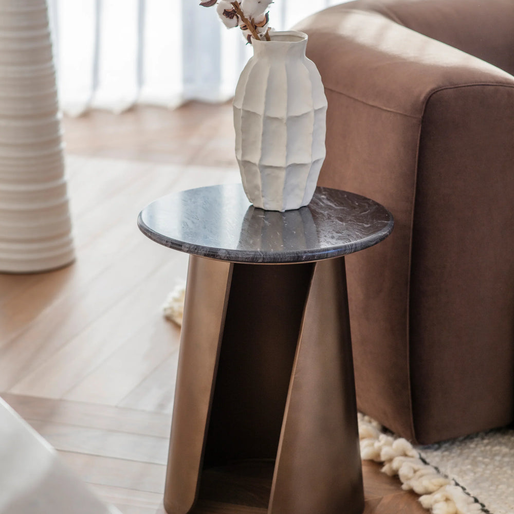 Bronze side table with marble top beside a brown sofa and white vase.