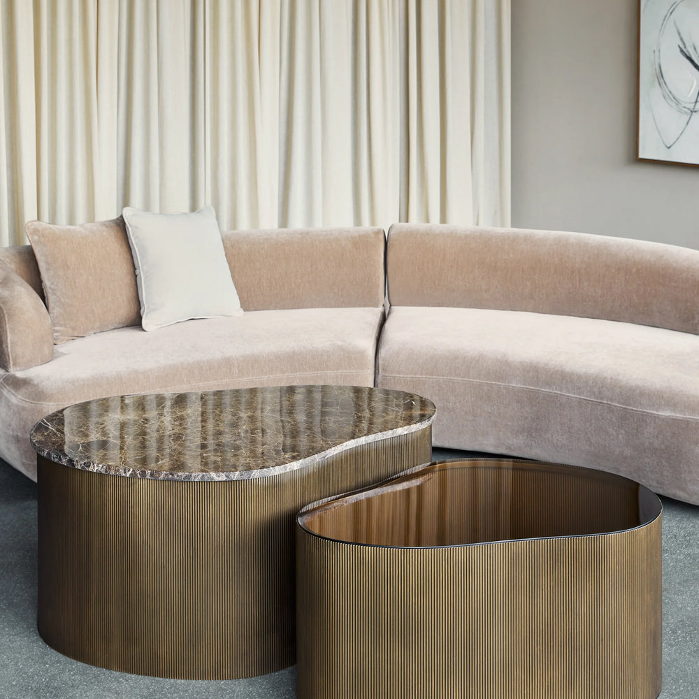 Curved marble and glass tables beside a beige sectional sofa.