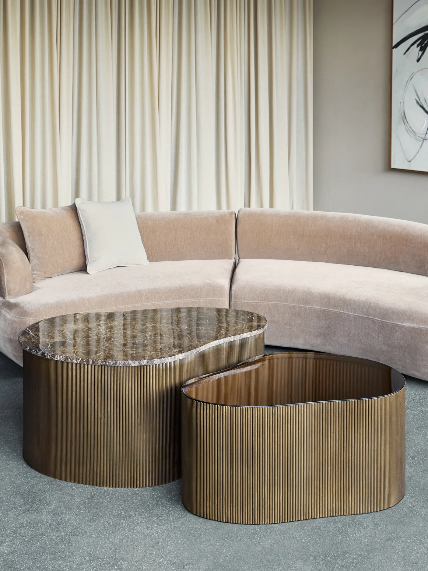 Curved marble and glass tables beside a beige sectional sofa.