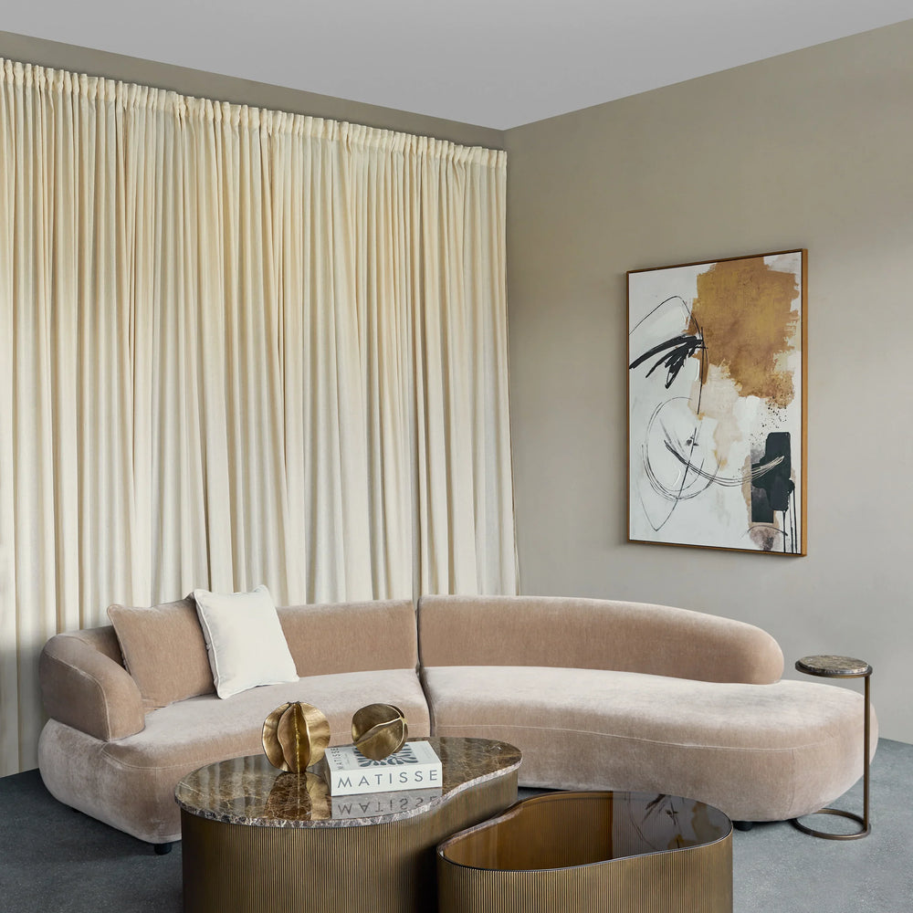 Bronze coffee tables in a modern living room with a curved beige sofa and abstract art.