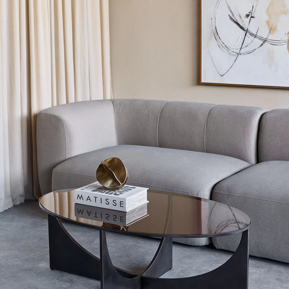 Black sculpted coffee table in modern living room with grey sofa and abstract art.