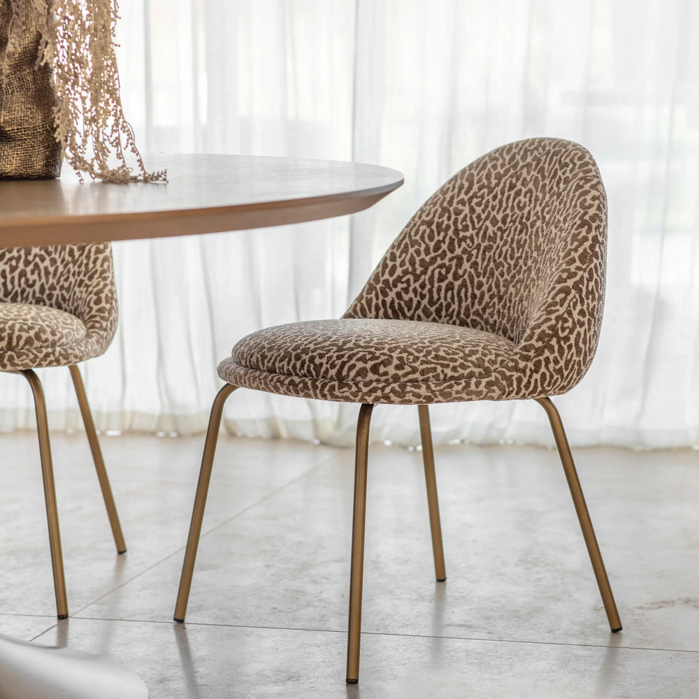 Leopard-patterned dining chair with gold legs beside a round table.