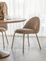 Leopard-patterned dining chair with gold legs beside a round table.