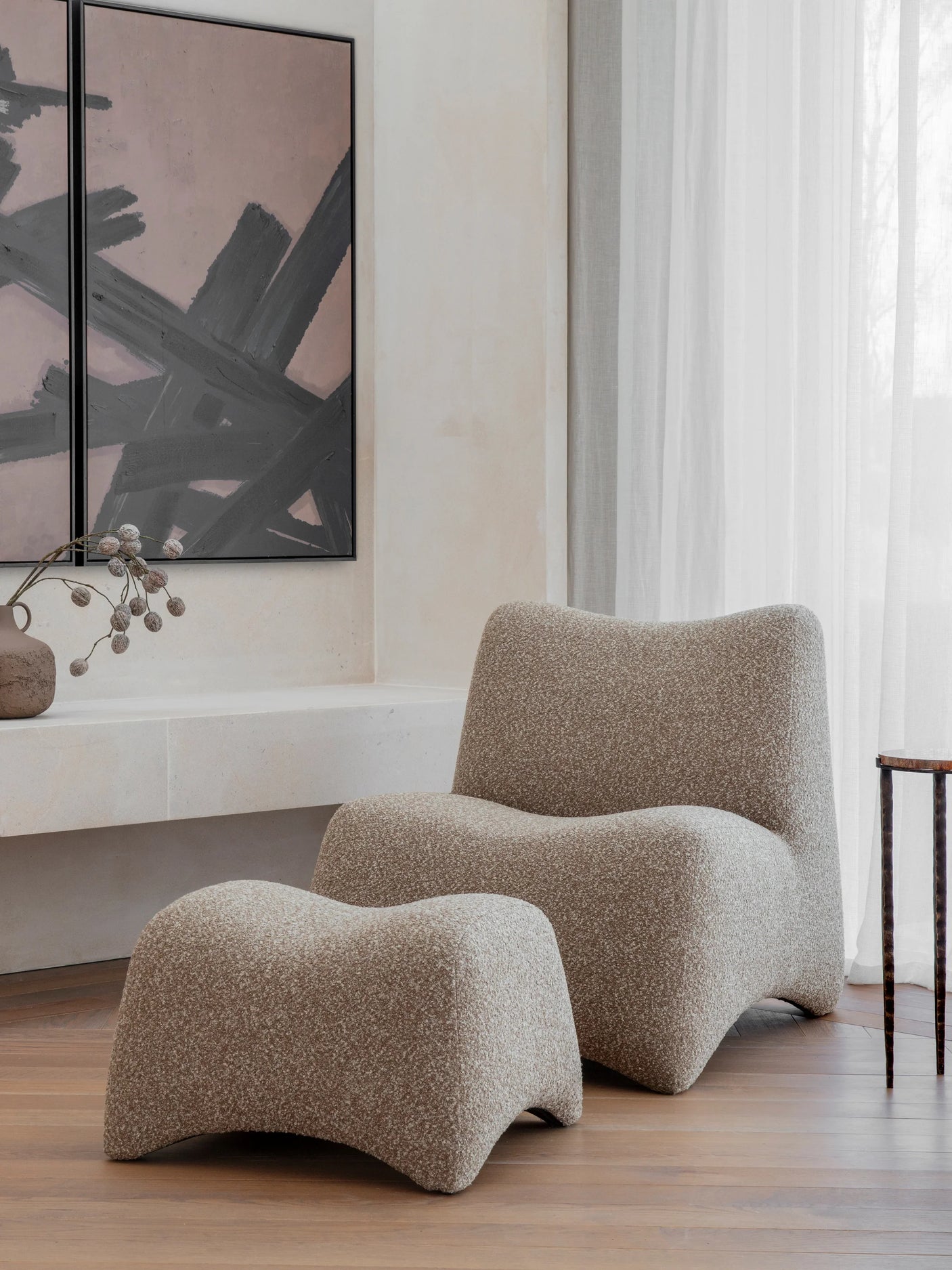 Curved beige chair and stool in modern living room with abstract art.