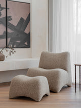 Curved beige chair and stool in modern living room with abstract art.