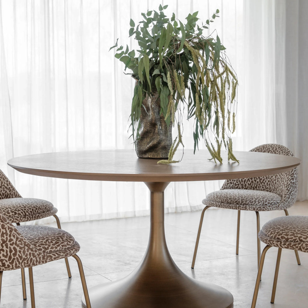 Bronze pedestal dining table with plant centerpiece and patterned chairs.