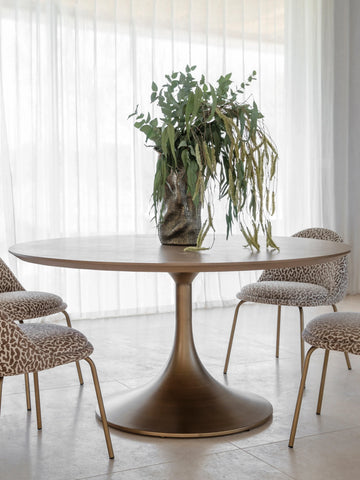 Bronze pedestal dining table with plant centerpiece and patterned chairs.
