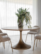 Bronze pedestal dining table with plant centerpiece and patterned chairs.