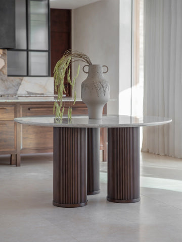 Marble-topped table with ribbed wooden legs in a sunlit dining room.