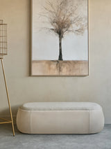 Beige upholstered bench beneath abstract tree painting in a minimalist room.