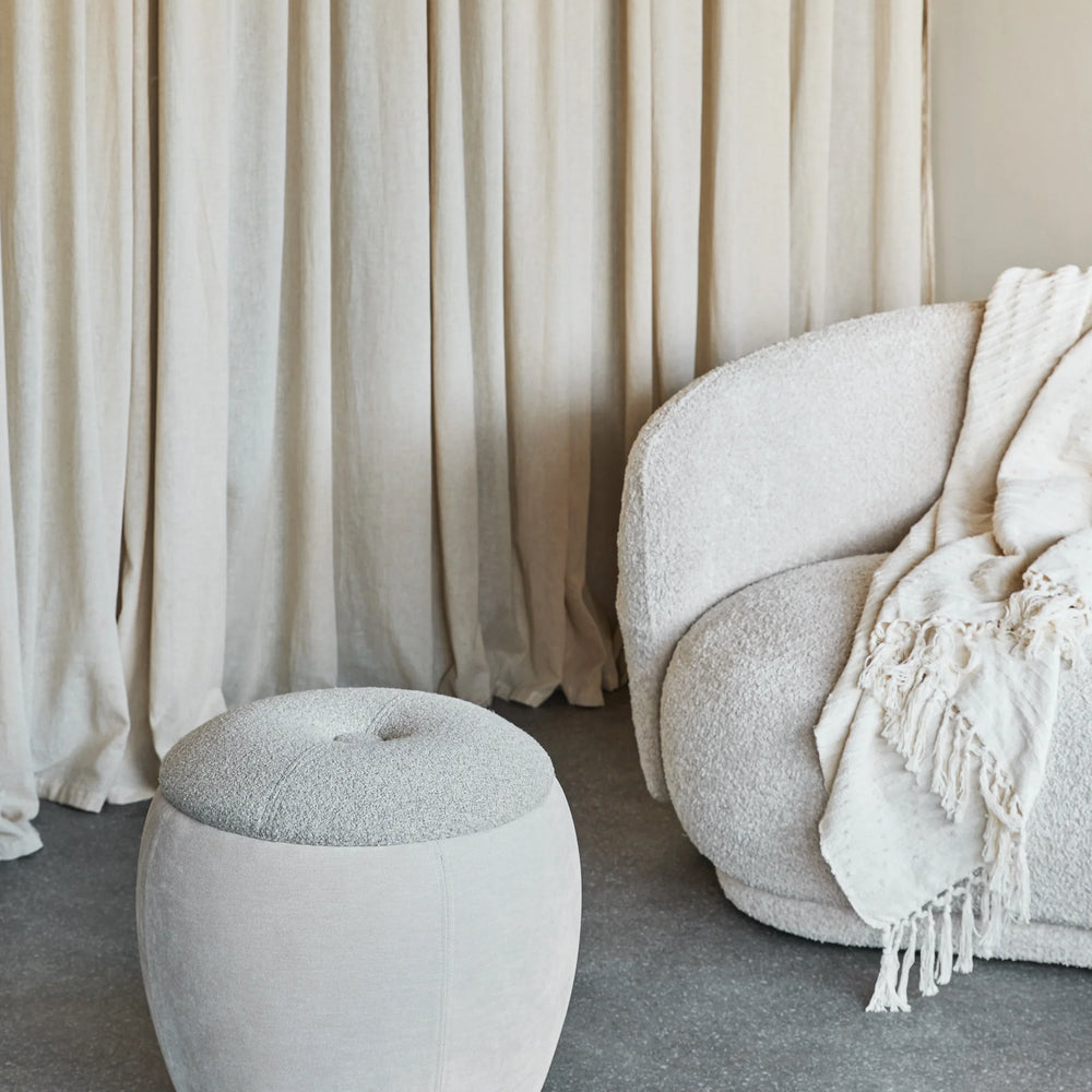 Beige storage stool in cozy living room with textured sofa and curtains.