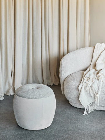 Beige storage stool in cozy living room with textured sofa and curtains.