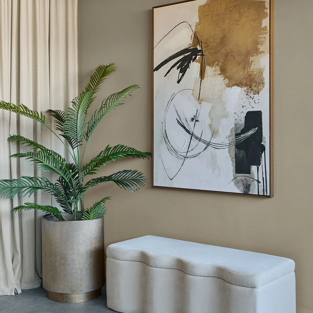 Cream fabric bench in modern room with abstract art and potted plant.