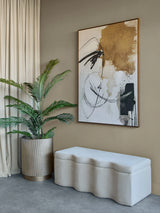 Cream fabric bench in modern room with abstract art and potted plant.