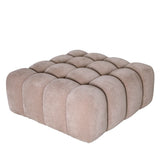 Beige upholstered pouf with tufted design and rounded edges.