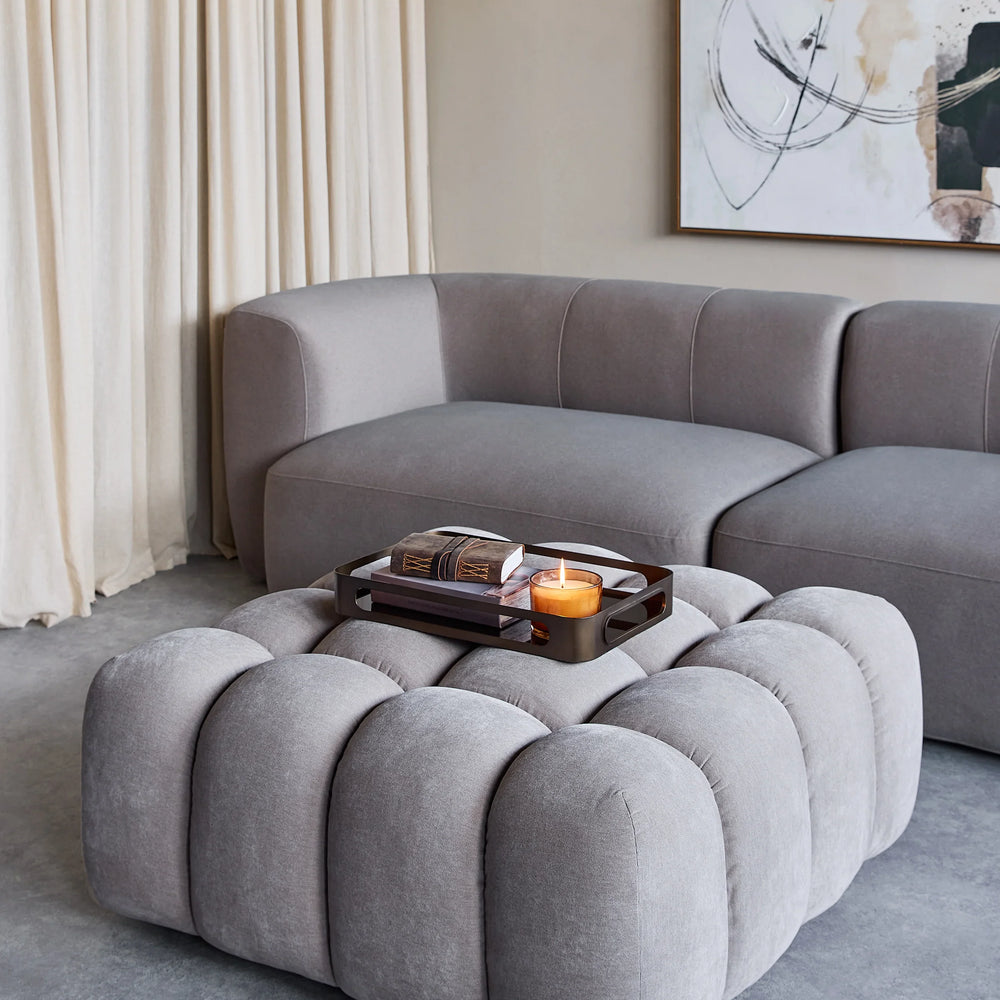 Grey upholstered pouf in modern living room with sofa and abstract art.