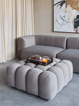 Grey upholstered pouf in modern living room with sofa and abstract art.