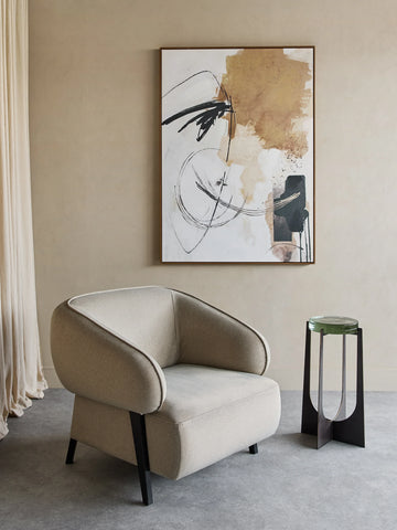 Beige armchair in modern room with abstract wall art and side table.