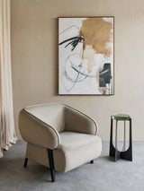 Beige armchair in modern room with abstract wall art and side table.