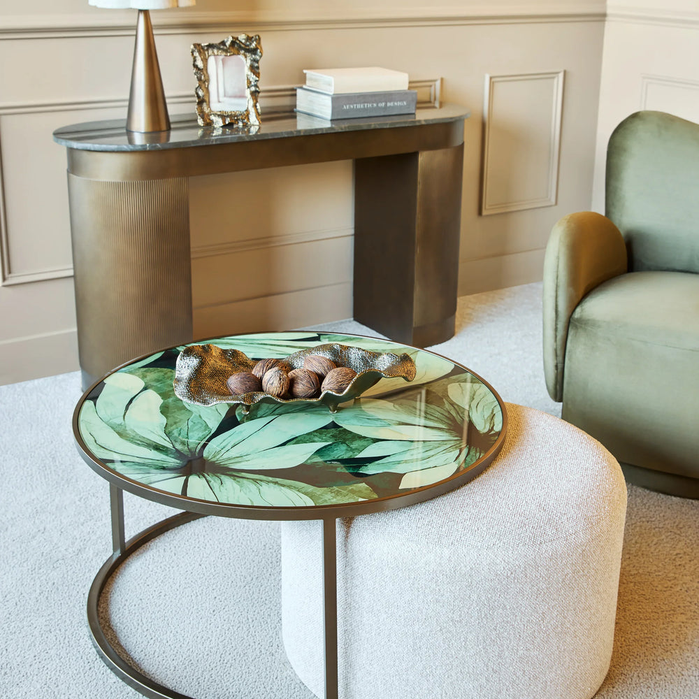 Leaf-patterned glass table with white pouffe in elegant living room setting.