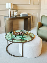 Leaf-patterned glass table with white pouffe in elegant living room setting.