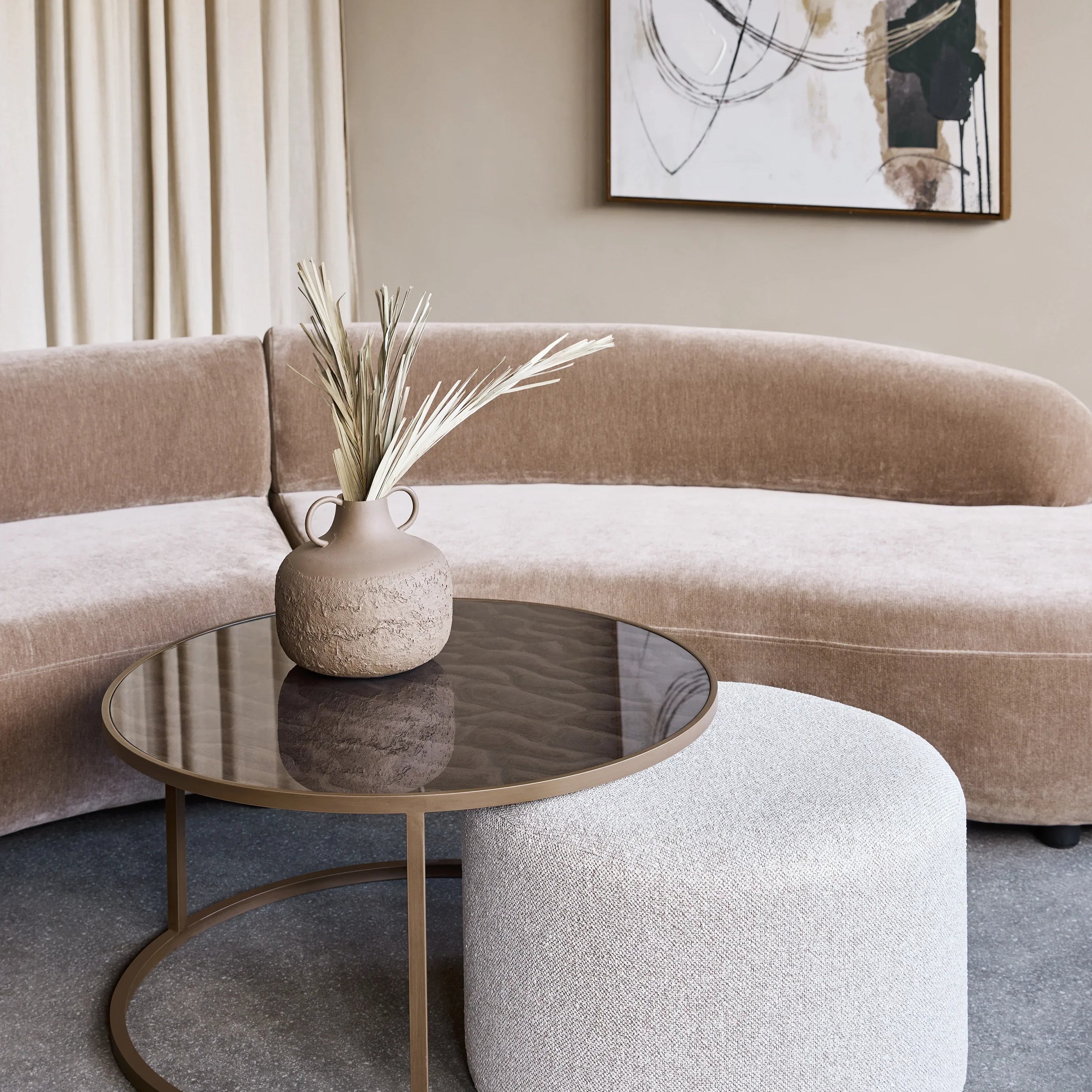 Round glass coffee table with textured pouffe in a modern living room setting.