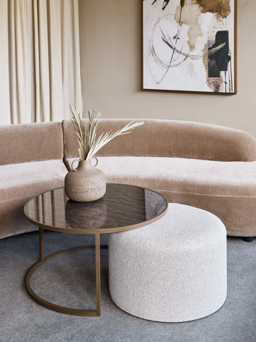 Round glass coffee table with textured pouffe in a modern living room setting.