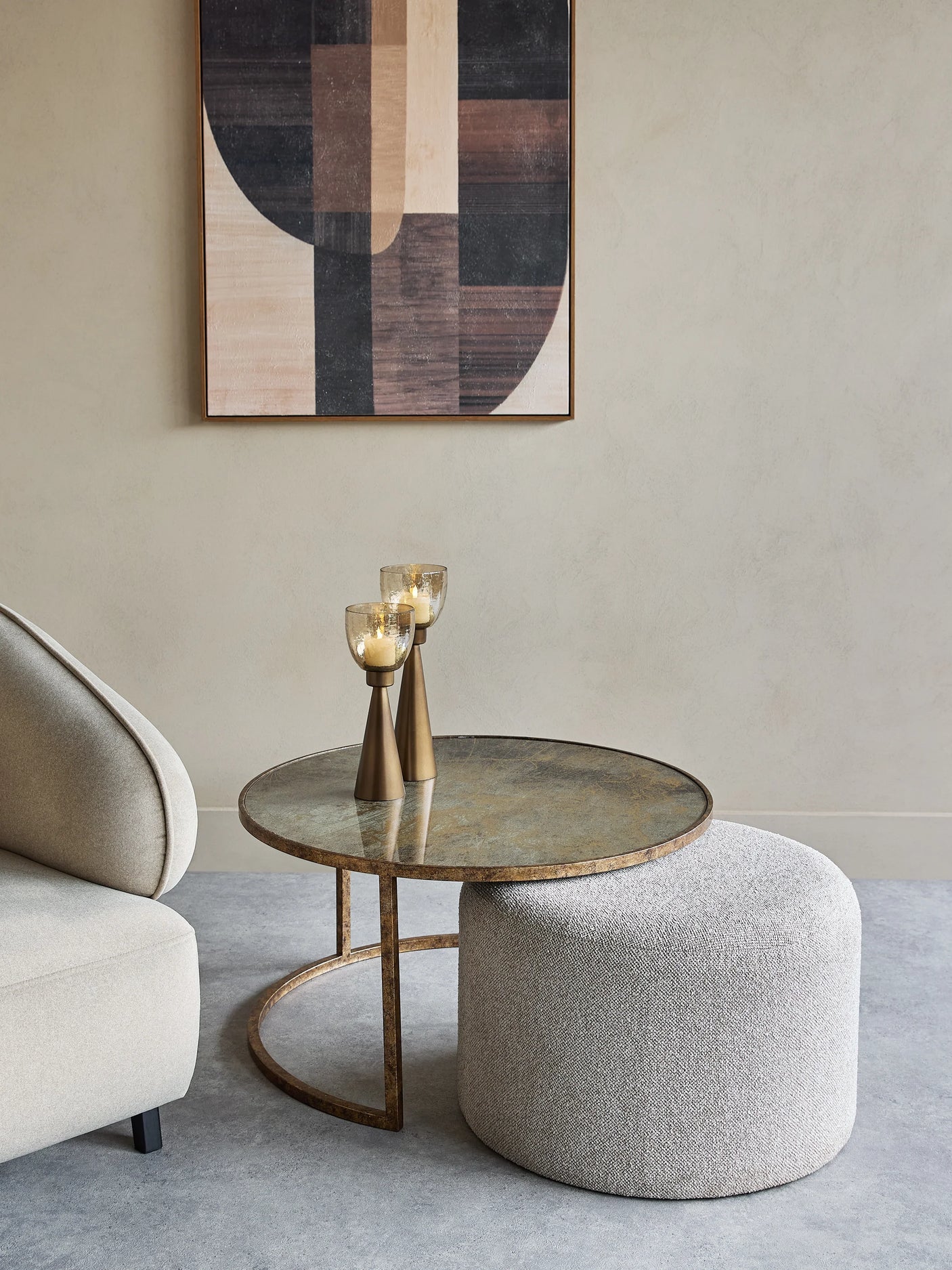 Round glass coffee table with bronze base beside a textured pouffe.