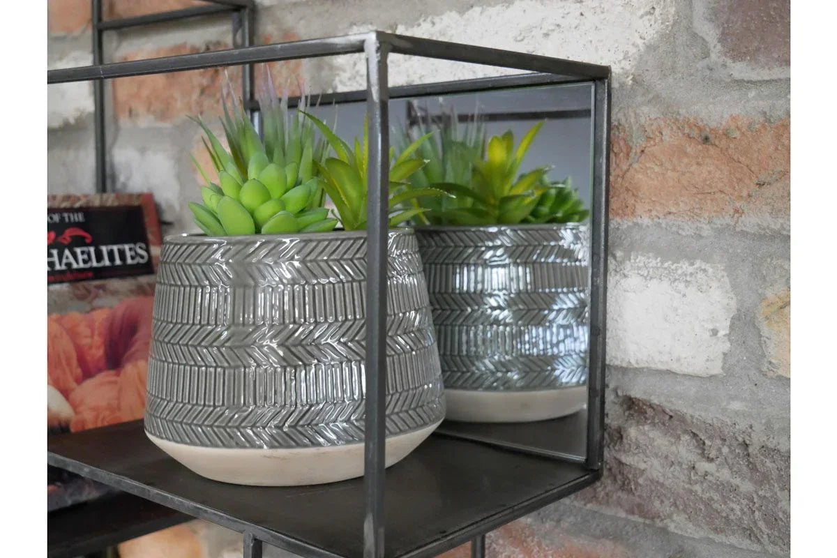 Grey ceramic plant pot with geometric pattern on wall shelf against exposed brick