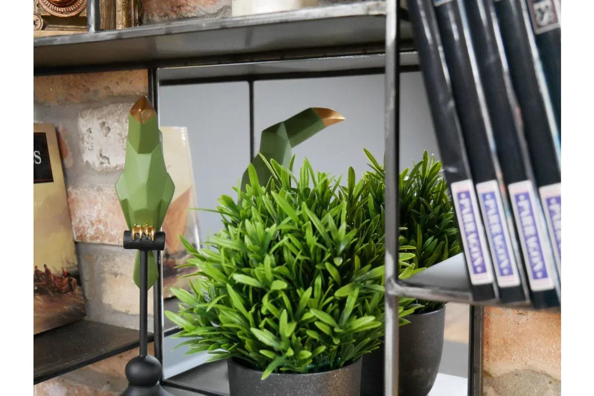 Green artificial plant in black pot beside geometric green bird ornament on shelf