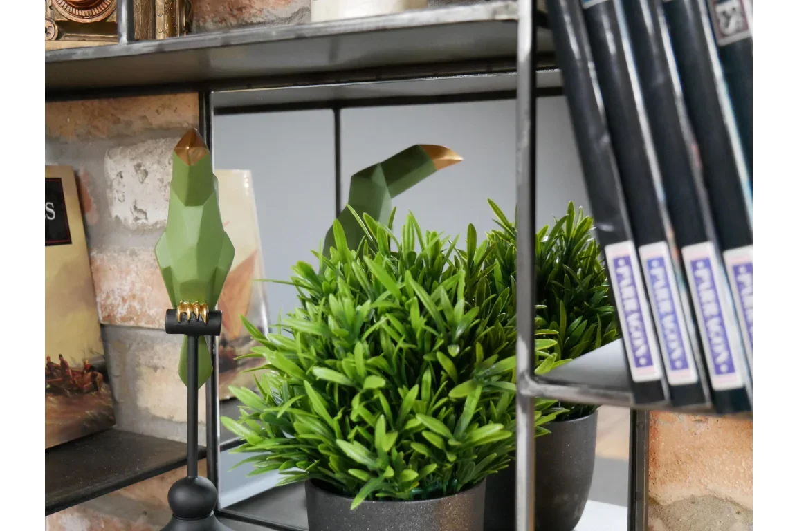 Artificial plant in black pot on shelf beside green geometric bird ornament and books