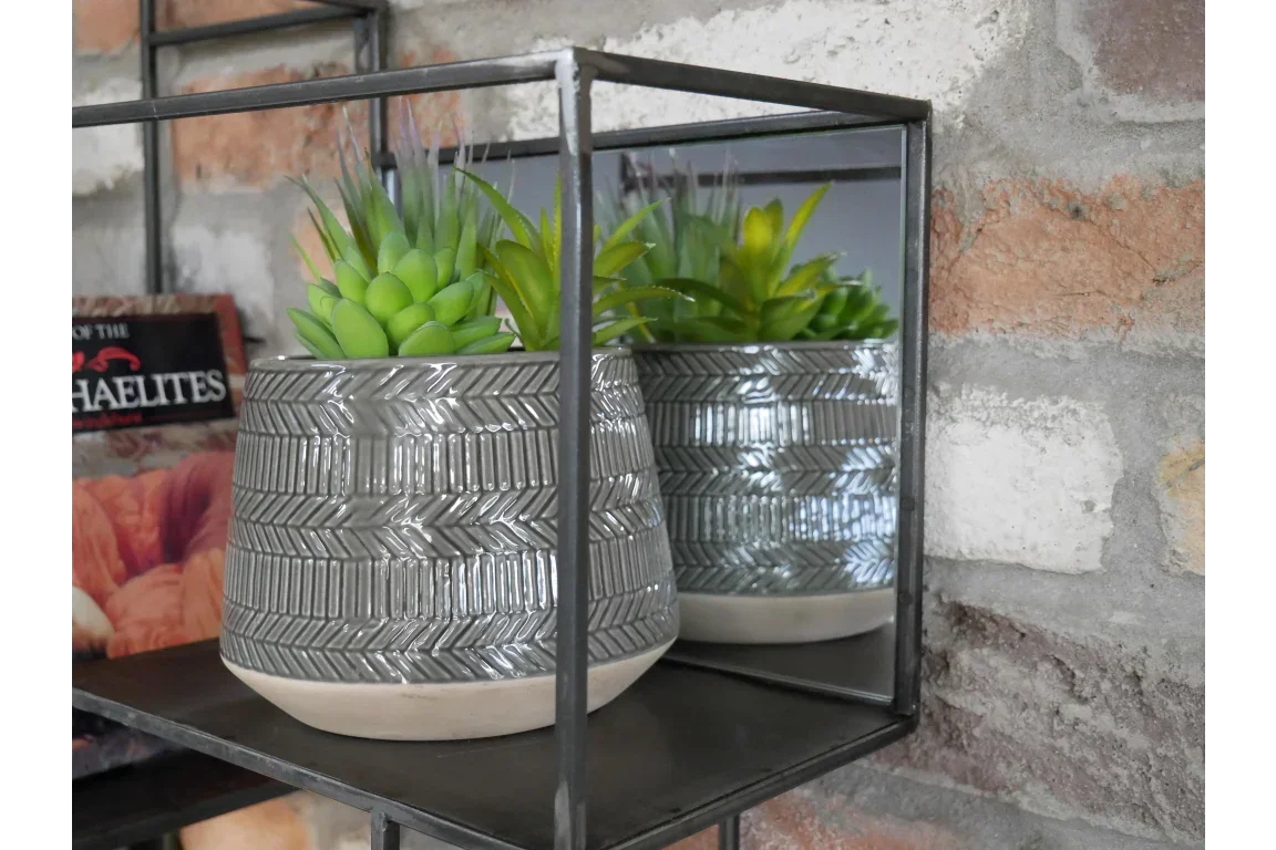 Grey ceramic plant pot with green artificial succulent on metal wall shelf against brick wall