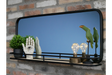 Black-framed rectangular wall mirror with wooden shelf featuring plant, decorative hands, light bulbs, and bird sculptures.