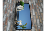 Rectangular black metal framed wall mirror with integrated shelf holding decor against a brick wall.