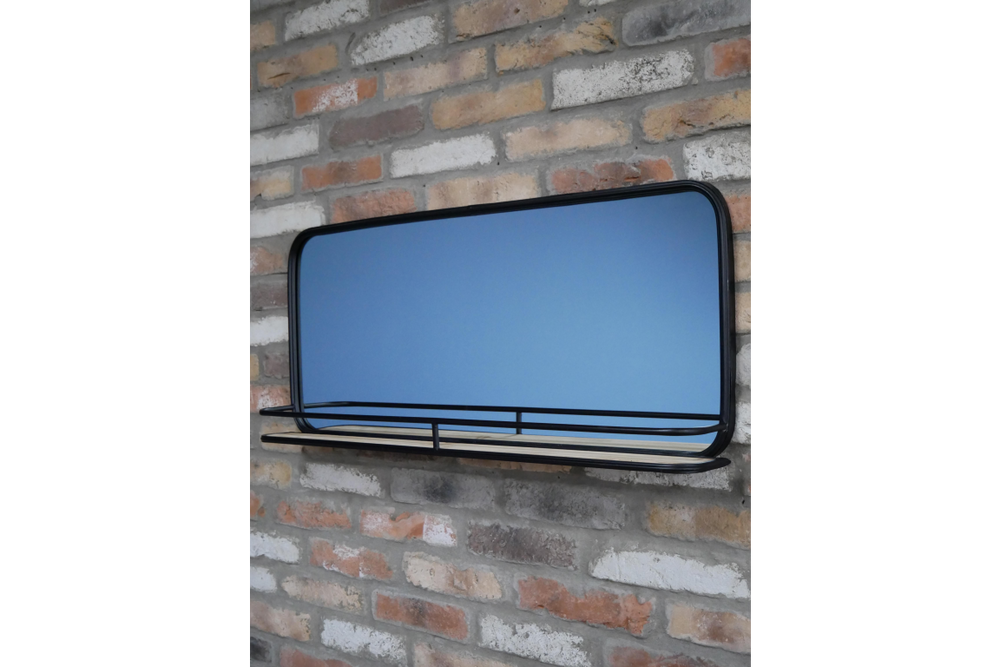 Wall-mounted rectangular mirror with black metal frame and wooden shelf in front, shown at slight angle.