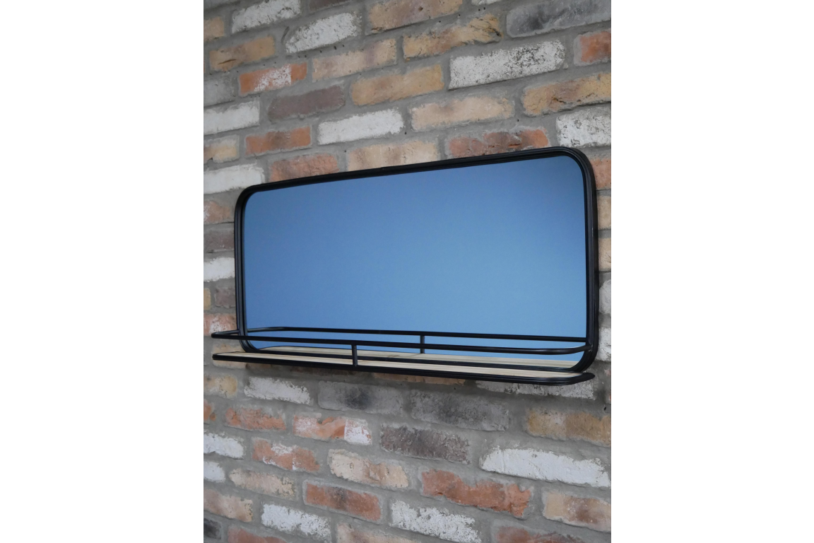 Wall-mounted rectangular mirror with black metal frame and wooden shelf in front, shown at slight angle.