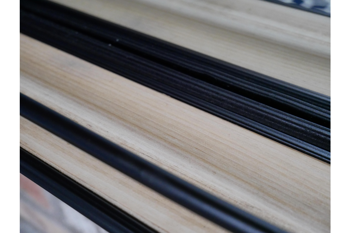 Close-up detail of light wood and black frame shelf edge on mirror with shelf at an angle.