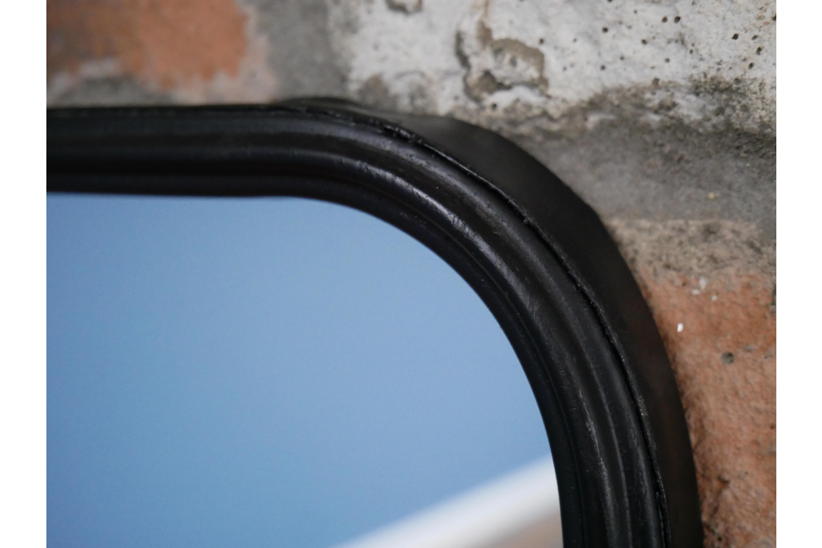 Close-up of black curved metal frame corner of rectangular mirror with a shelf against a textured wall.