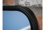 Close-up of black curved metal frame corner of rectangular mirror with a shelf against a textured wall.