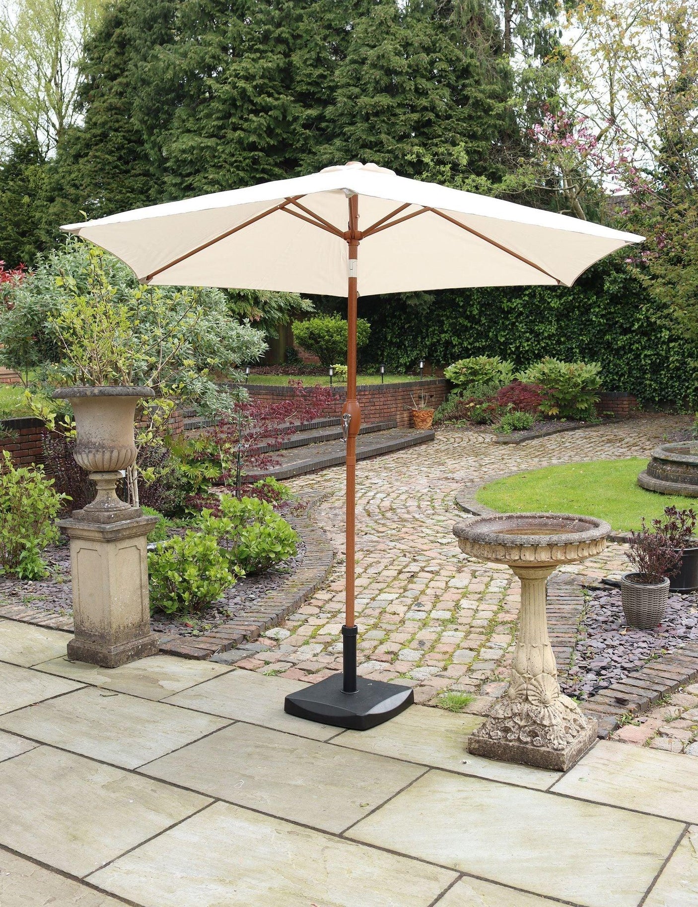 Cream outdoor parasol with wooden pole on stone patio in garden setting